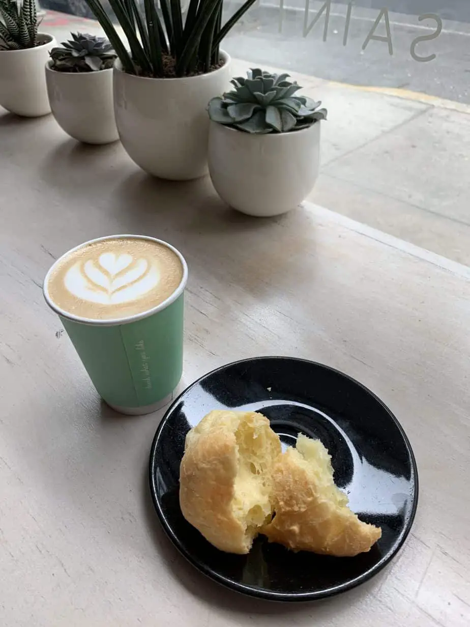 A cup of coffee with a half eaten cheese bread