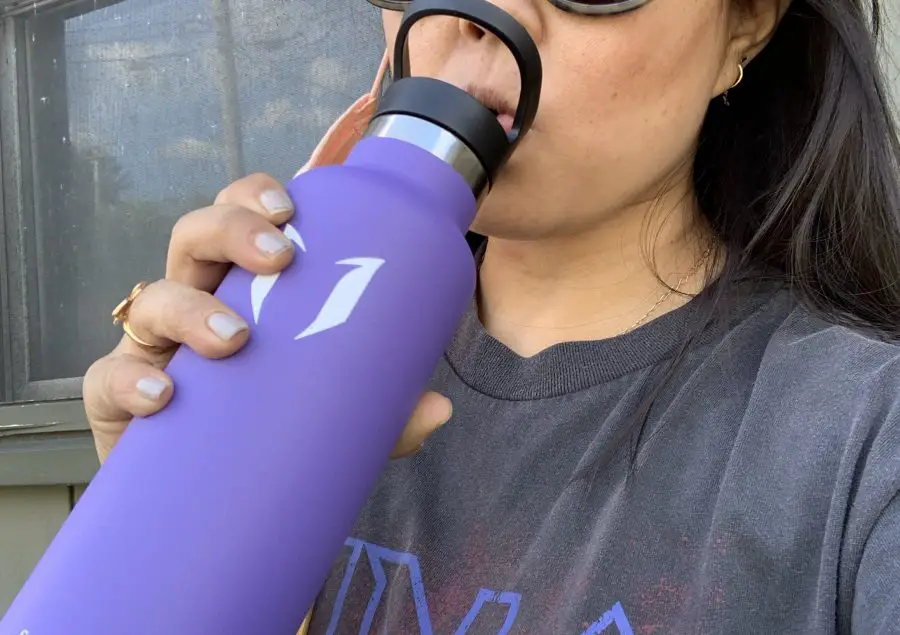 Girl in sunglasses drinking from a purple bottle
