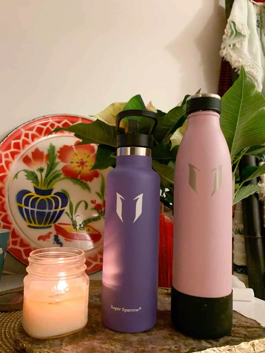Pink and purple water bottle next to a lit candle 